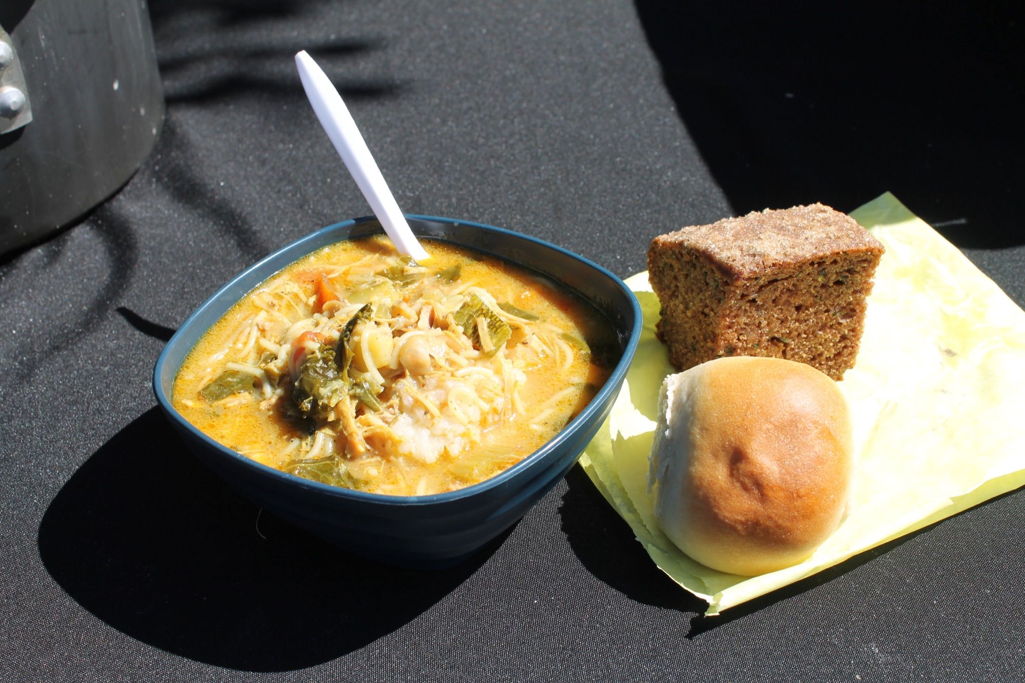 A bowl of vegetable soup with a bread roll and a slice of brown bread on a paper napkin