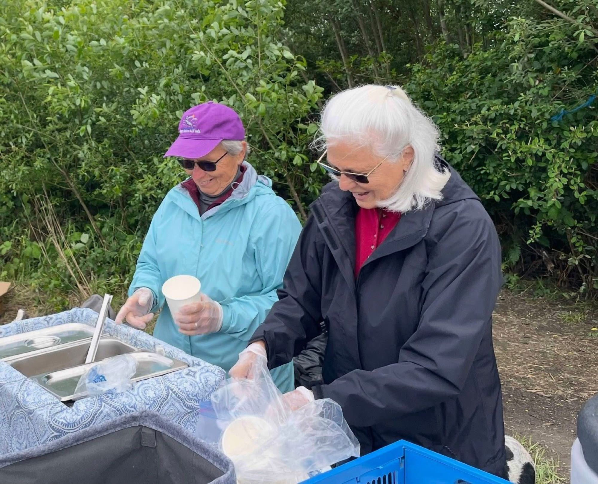 Two volunteers smiling as they serve soup into paper cups